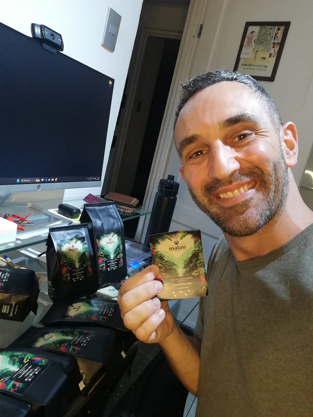 Mattia, fundador de Malau Coffee, sentado en una oficina y sosteniendo una etiqueta, con bolsas de café a su alrededor.